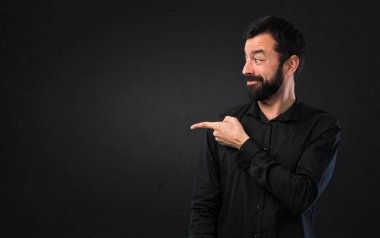 Siyah arka planda lateral işaret eden sakallı yakışıklı adam