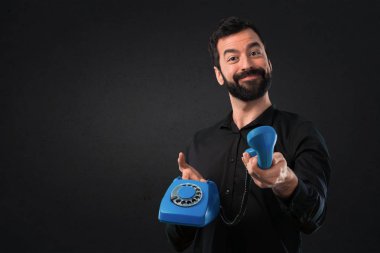 Siyah arka plan üzerine konuşmak için vintage telefon sakallı yakışıklı adam