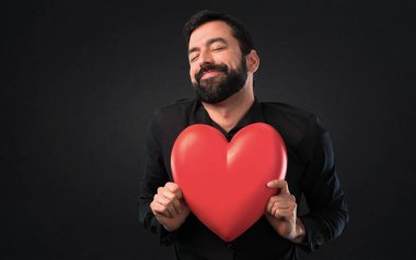 Siyah arka plan üzerine tutmak bir kalp oyuncak sakallı yakışıklı adam