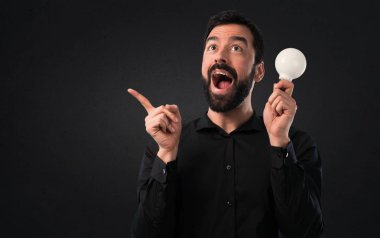 Bir ampul siyah arka plan üzerine tutarak sakallı yakışıklı adam