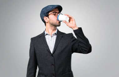 Gri arka plan üzerinde götürmeye yakışıklı modern adam bere ve kahve tutan gözlük