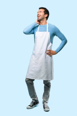 Ayakta ve mavi arka plan üzerinde kafa çizilmemesi iken bir fikir düşünce bir önlük giyen adamın tam vücut