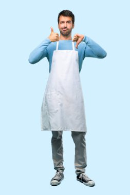 Tam vücut iyi-kötü işaret yapma bir önlük giyen adam. Kararsız kişi Evet arasında veya mavi arka plan üzerinde değil