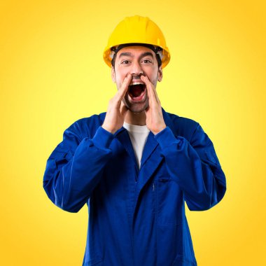 Geniş açık ağız ile bağırarak ve sarı zemin üzerine bir şey ilan kask ile genç işçi