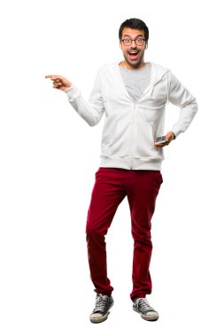 Bir adam gözlük ve parmak tarafına işaret ve kendinden emin bir poz beyaz arka plan üzerinde gülümseyen iken bir ürün sunan dinleme müzik tam uzunlukta bir kadeh