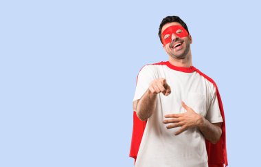 Birisi parmak ile işaret ve çok izole mavi arka plan üzerinde gülüyor maskesi ve kırmızı pelerin adamla süper kahraman