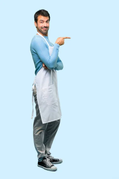 손가락을 가리키는 파란색 배경에 위치에 제품을 앞치마를 남자의 — 스톡 사진