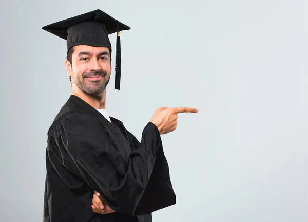 彼の卒業の日大学側に指を指していると灰色の背景に側臥位で製品を提示の男 — ストック写真