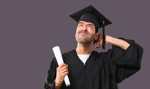 疑問を持つ彼の卒業日大学と紫色の背景に頭を掻きながら混乱表情の男 — ストック写真