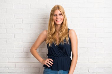 Silah, kalça ile poz ve beyaz tuğla duvar arka plan üzerinde gülümseyen sarışın kadın