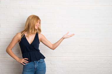 Sarışın kadın geri üzerinde beyaz tuğla bir ürün sunan işaret parmağı ile işaret duvar arka plan