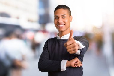 Jest Yaşasın vererek ve şehrin ortasında gülümseyen genç Afro-Amerikan adam