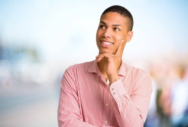 Ayakta ve odaklanmamış açık arka plan üzerinde ararken bir fikir düşünme genç Afro-Amerikan adam