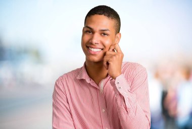 Odaklanmamış açık arka plan üzerinde tatlı bir ifade ile gülümseyen genç Afro-Amerikan adam