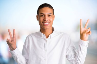 Gülümseyen ve zafer işareti iki elle ve neşeli bir yüz ile odaklanmamış açık arka plan üzerinde gösterilen genç Afro-Amerikan adam