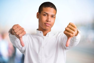 Başparmak aşağı her iki el ile gösterilen genç Afro-Amerikan adam. Odaklanmamış açık arka plan üzerinde negatif ifade