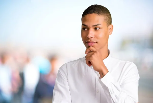Young african american man standing and looking to the side with the hand on the chin on unfocused outdoor background