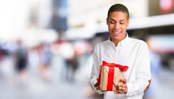 年轻的非洲裔美国人男子与白色衬衫持有礼品盒在手在城市中部 — 图库照片