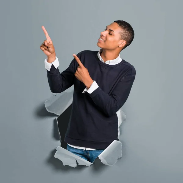 Young african american man pointing with the index finger a great idea and looking up through a paper hole