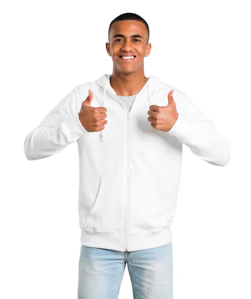 深色皮肤的年轻人与白色卫衣给予竖起大拇指的手势和微笑 因为有成功在孤立的白色背景 — 图库照片