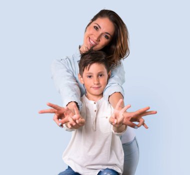 Anne ve kızı gülümseyen ve zafer gösterilen mavi arka plan üzerinde oturum