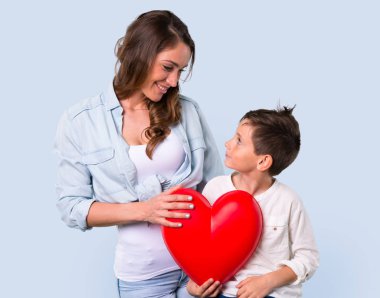 Anne ve kızı tutmak büyük kalp simgesi oyuncak mavi arka plan üzerinde