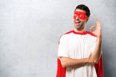 Süper kahraman maske ve kırmızı pelerin dokulu gri arka plan üzerinde bir göz kırptı süre parmak ok işaretiyle gösterilen adamla