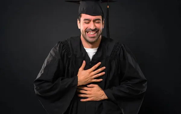 黒い背景に胸に手を置いている間多くを笑って彼の卒業日大学の男 — ストック写真