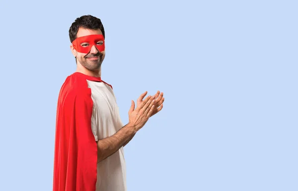 Superhero man with mask and red cape applauding after presentation in a conference on isolated blue background