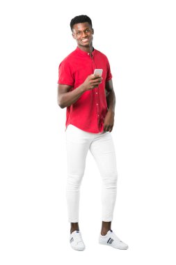 Kameraya bakarak ve beyaz arka plan üzerinde mobil kullanırken gülümseyen genç Afro-Amerikan insanın tam vücut