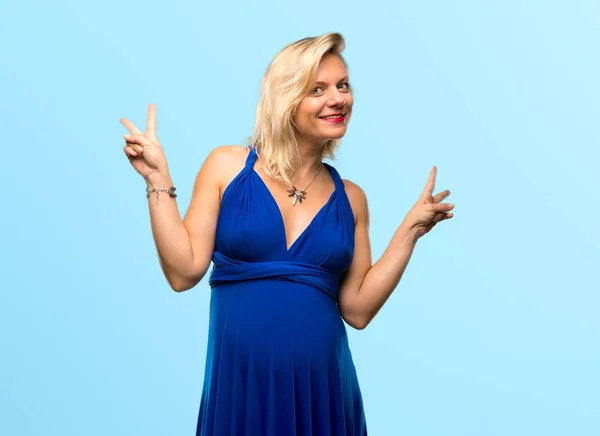 Kobieta Ciąży Blondynka Niebieską Sukienkę Uśmiechając Się Pokazuje Znak Zwycięstwa — Zdjęcie stockowe