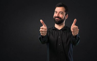 Siyah arka plan üzerine başparmak ile sakallı yakışıklı adam
