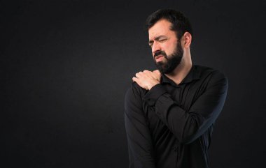 Siyah arka plan üzerinde omuz ağrısı ile sakallı yakışıklı adam