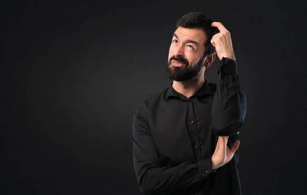 Handsome man with beard having doubts on black background