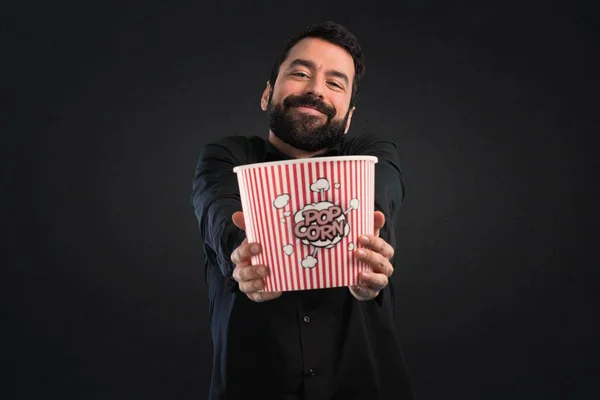 Handsome man with beard eating popcorns on black background
