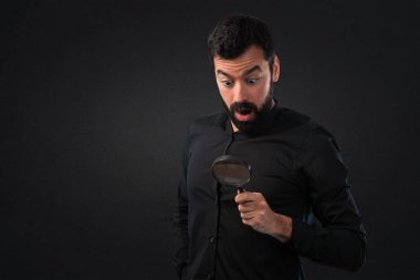 Siyah arka plan üzerine büyüteç ile sakallı yakışıklı adam