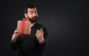 Siyah arka plan üzerine bir hediye tutarak sakallı yakışıklı adam