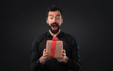 Siyah arka plan üzerine bir hediye tutarak sakallı yakışıklı adam