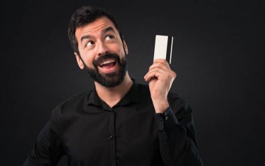 Siyah arka plan üzerine bir kredi kartı tutan sakallı yakışıklı adam