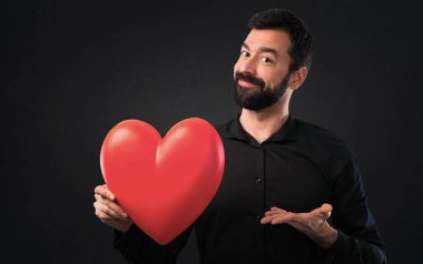 Siyah arka plan üzerine tutmak bir kalp oyuncak sakallı yakışıklı adam