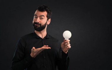 Bir ampul siyah arka plan üzerine tutarak sakallı yakışıklı adam