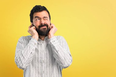 Her iki kulak elleriyle kapsayan sakallı yakışıklı adam