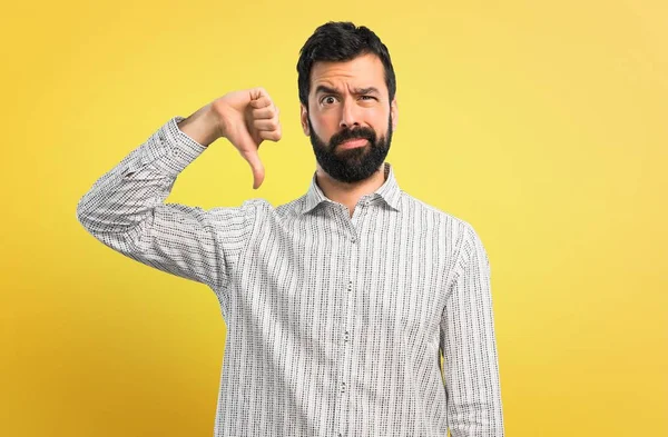 Başparmak aşağı negatif ifade işaretiyle gösterilen sakallı yakışıklı adam