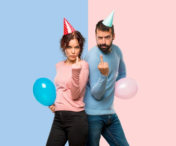 Casal Com Balões Chapéus Aniversário Fazendo Gesto Chifre Expressão Negativa — Fotografia de Stock