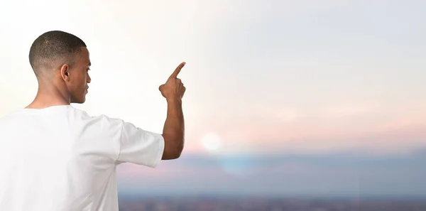 Young african american man pointing back with the index finger on sunset background