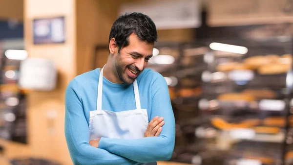 Man wearing an apron keeping the arms crossed while smiling in a bakery