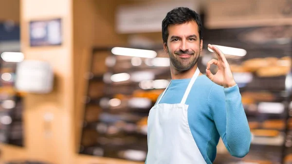 Man wearing an apron showing an ok sign with fingers. Face of happiness and satisfaction in a bakery