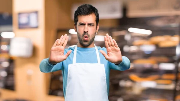 Man wearing an apron making stop gesture with her hand for disappointed with an opinion in a bakery