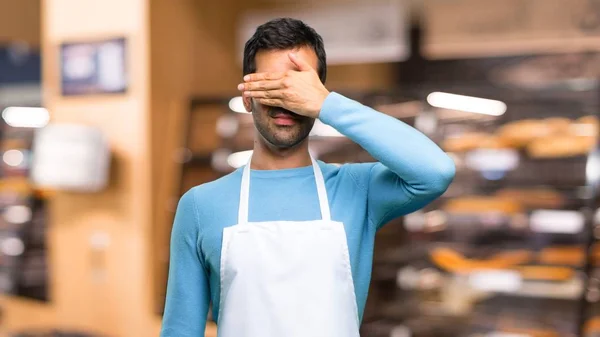 Man wearing an apron covering eyes by hands. Do not want to see something in a bakery