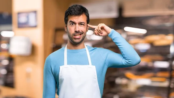 Man wearing an apron making the gesture of madness putting finger on the head in a bakery